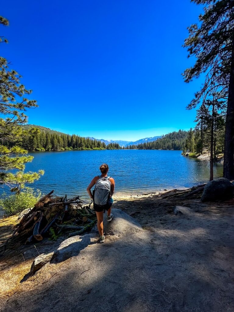 Blue water of Hume Lake with a hiker standing in the foreground and mountains in the distance.