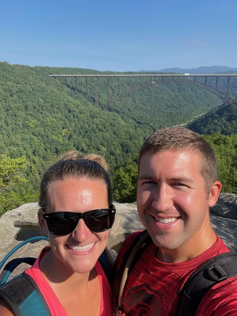 Two hikers stand on the Long Point Trail with the New River Bridge in the background.