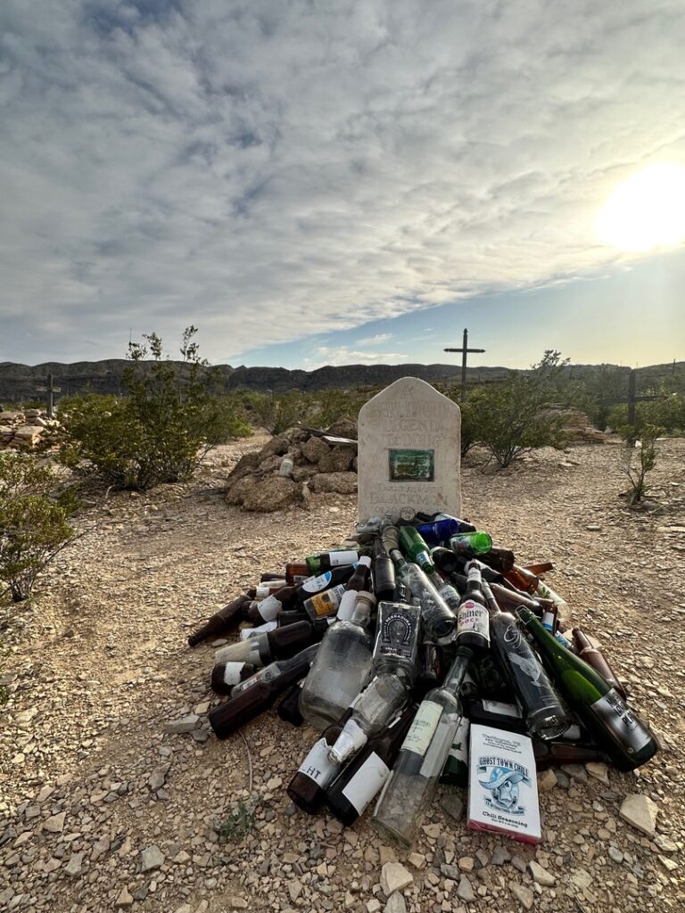 Another gravestone at the cemetery with glass bottles piled up nearby.