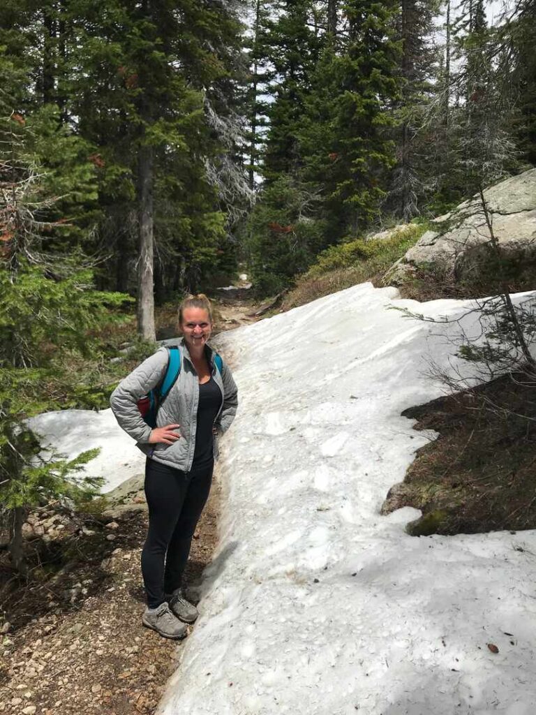 A hiker poses next to a large snow drift on the North Fork Cascade Canyon Trail.