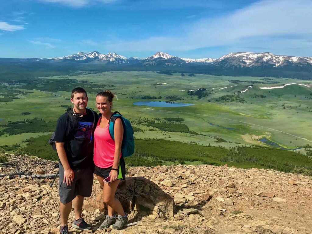 Two hikers post at the Bunsen Peak summit with the amazing mountains in the distance.