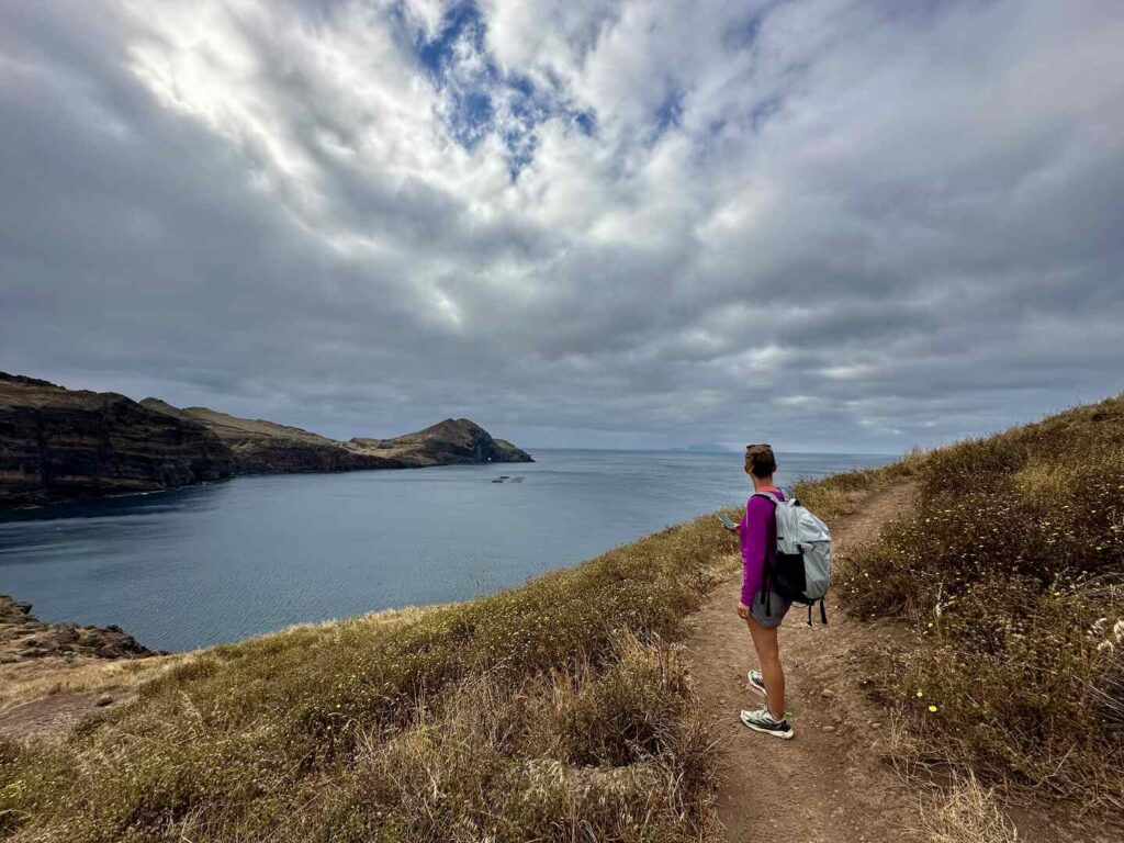 A hiker stands overlooking D'Abra Bay on the PR8 trail in Madeira on a cloudy day.