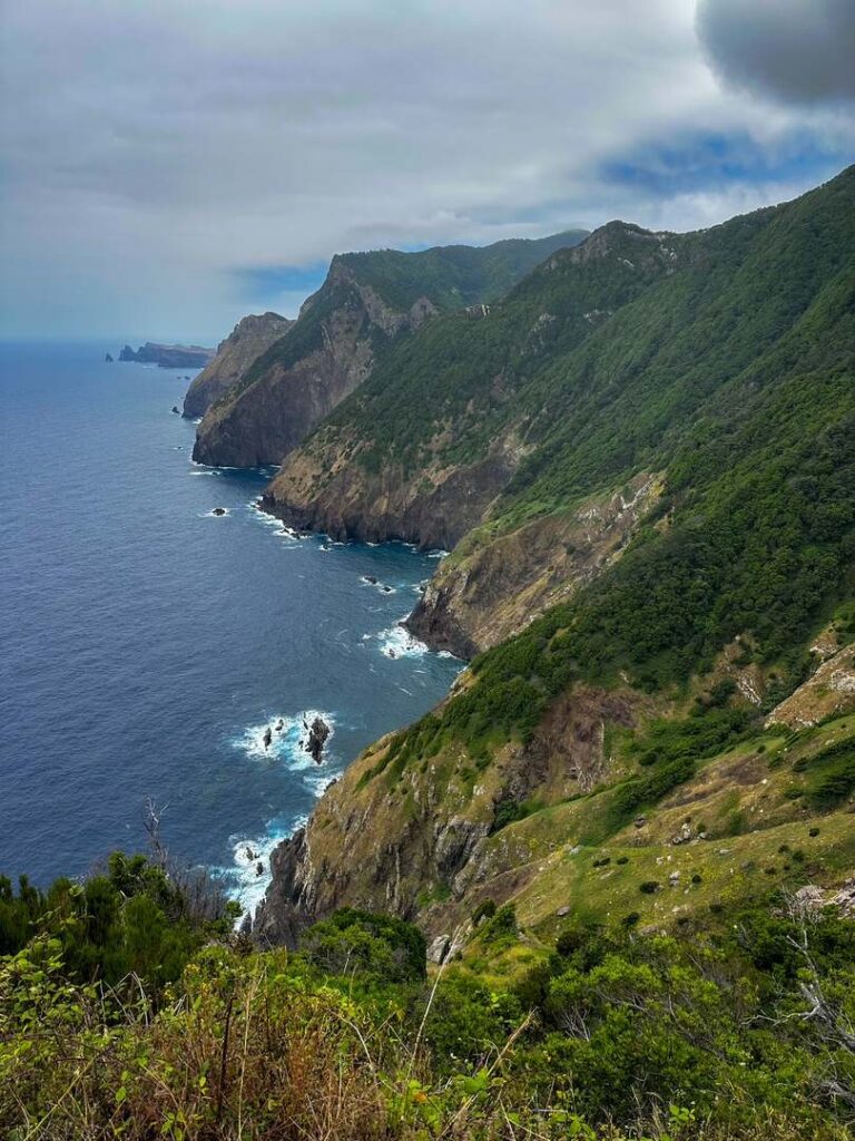 A view overlooking the green and rocky cliffs that plunge into the blue ocean below.