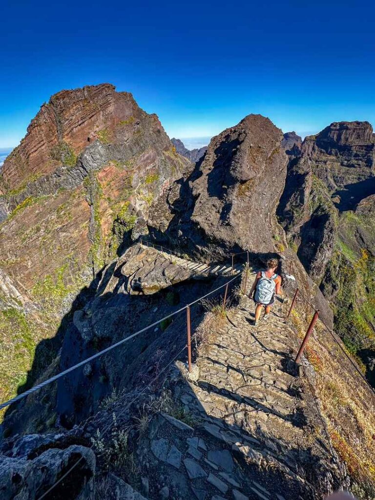 A hiker walking down a steep set of stairs with sheer drop offs on both sides of the trail.