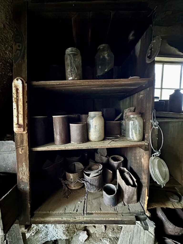 Many old artifacts sit inside the boulder house on shelves including tin cans, glass jars, and bottles.